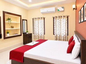 Een hotelkamer met een bed, een plank met decoratieve objecten, een airconditioner en gordijnen.