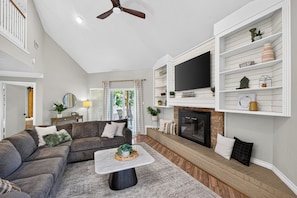 A living room with a sofa, coffee table, fireplace, TV, and shelves. - Charming Spacious Retreat - 5 mins from The Woodlands Mall & i45 (Conroe)