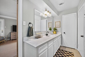A modern bathroom with a white vanity, a large mirror, a sink, and a shower area. - Charming Spacious Retreat - 5 mins from The Woodlands Mall & i45 (Conroe)
