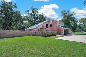 A single-story brick house with a sloped roof, a front garage, and a wooden fence. - Charming Spacious Retreat - 5 mins from The Woodlands Mall & i45 (Conroe)