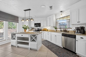 A modern kitchen with white cabinetry, a central island, stainless steel appliances, and a large window providing natural light. - Charming Spacious Retreat - 5 mins from The Woodlands Mall & i45 (Conroe)