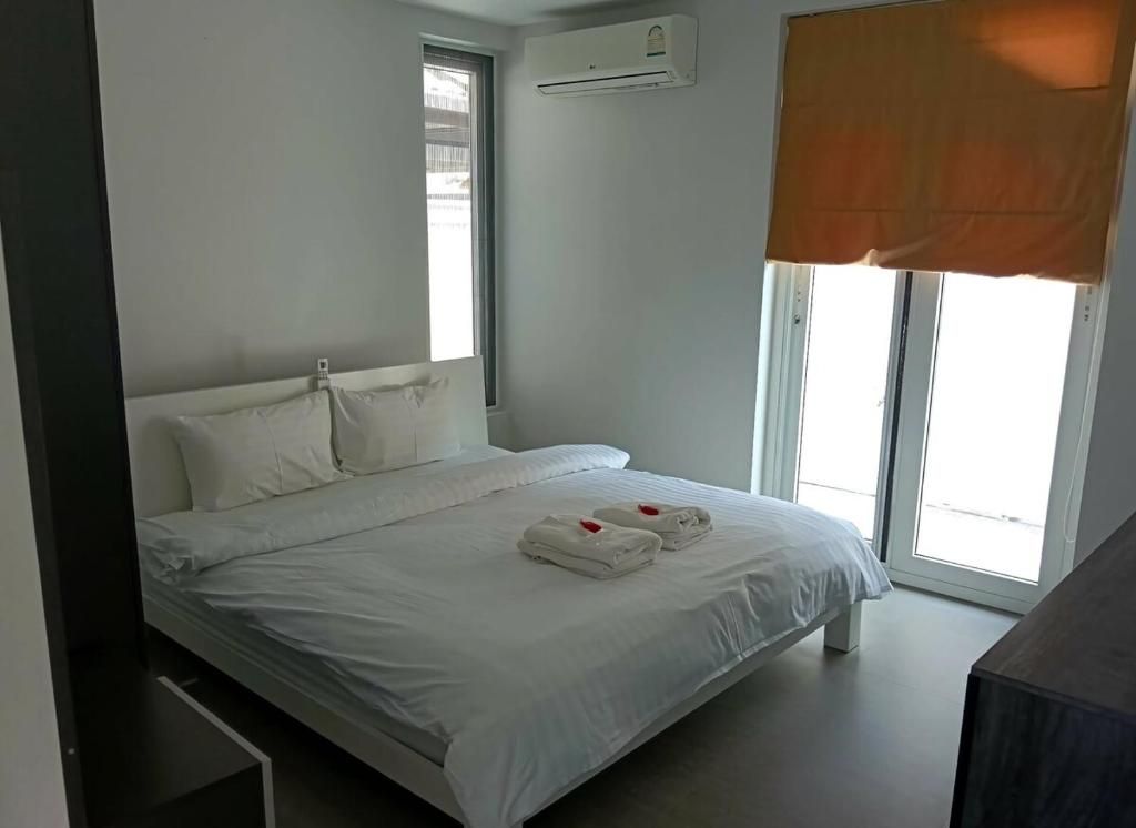 Een slaapkamer met een bed, witte lakens, een raam met zonwering en een airconditioning.