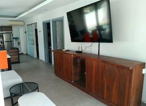 Un saló modern amb un televisor de pantalla plana muntat sobre un moble de fusta, una taula de centre de vidre i un sofà blanc.