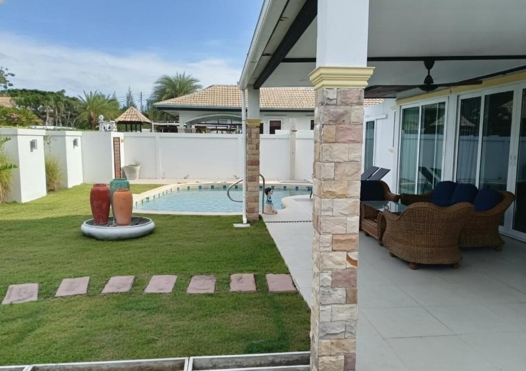 A covered outdoor area with a swimming pool, a lawn, and outdoor furniture.