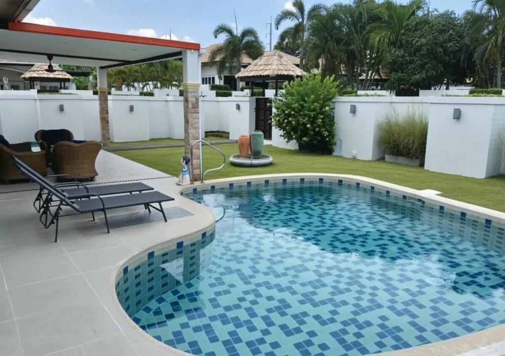 A swimming pool with a tiled edge, surrounded by a covered patio area with lounge chairs.
