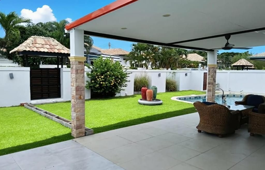 A covered patio area with a pool, outdoor furniture, and a well-maintained lawn.