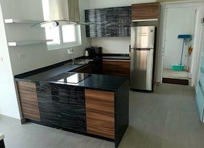 Et moderne køkken med en central ø, rustfrie hvidevarer og en mørk bagplade.
