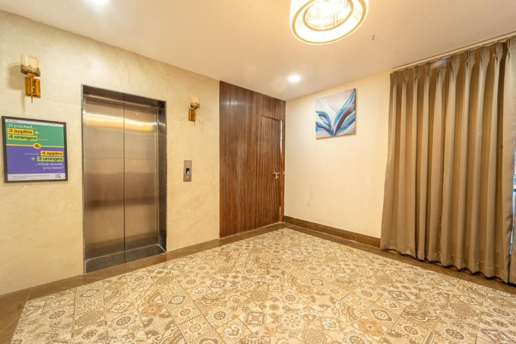A hotel lobby with an elevator, a wooden door, patterned carpet, and a painting on the wall.
