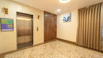 A hotel lobby with an elevator, a wooden door, patterned carpet, and a painting on the wall.