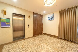 A hotel lobby with an elevator, a wooden door, patterned carpet, and a painting on the wall. - Treebo Golden Palm, Civil Lines (Jabalpur)