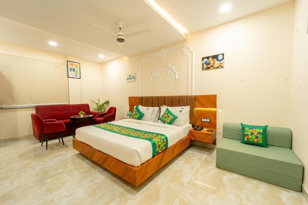 Una habitación de hotel con una cama, un sillón rojo, un sofá verde, una mesita y un teléfono instalado en la pared.