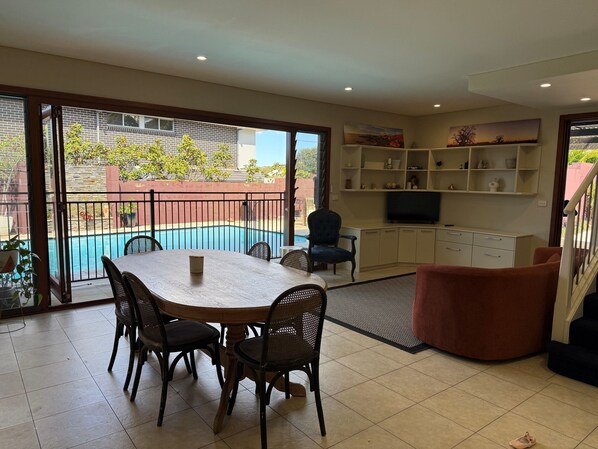 A spacious living area with a pool, a dining table with chairs, a sofa, a TV on a shelf, and a staircase. - House with own private pool, an easy walk to the Beach, Restaurants and Cafe's (Cronulla)