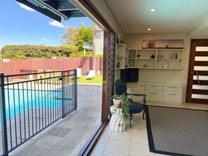 A pool area with a fence, a chair, a potted plant, and a television in a room with shelves and a door. - House with own private pool, an easy walk to the Beach, Restaurants and Cafe's (Cronulla)