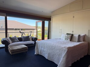 A bedroom with a large bed, a sofa, and a view of a brick building through a sliding door. - House with own private pool, an easy walk to the Beach, Restaurants and Cafe's (Cronulla)