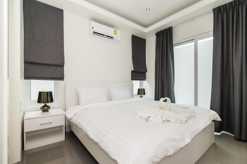 A hotel room with a large bed, a bedside table with a lamp, an air conditioning unit, and a window with curtains.