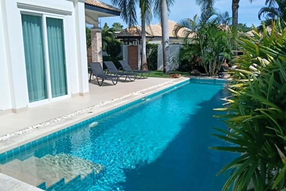 A swimming pool with clear blue water, surrounded by lounge chairs and palm trees.