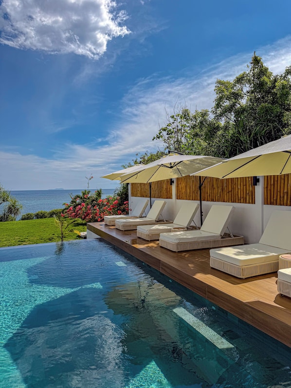 An infinity pool with lounge chairs and umbrellas, overlooking a body of water and greenery. - Villa Nindot - Private Pool Villas - Adult only (San Juan)