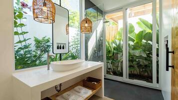 A modern bathroom with a large window, a white sink, and wicker pendant lights.