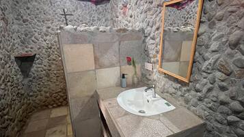 A bathroom with a stone wall, a sink, a mirror, and a red checkered cloth.