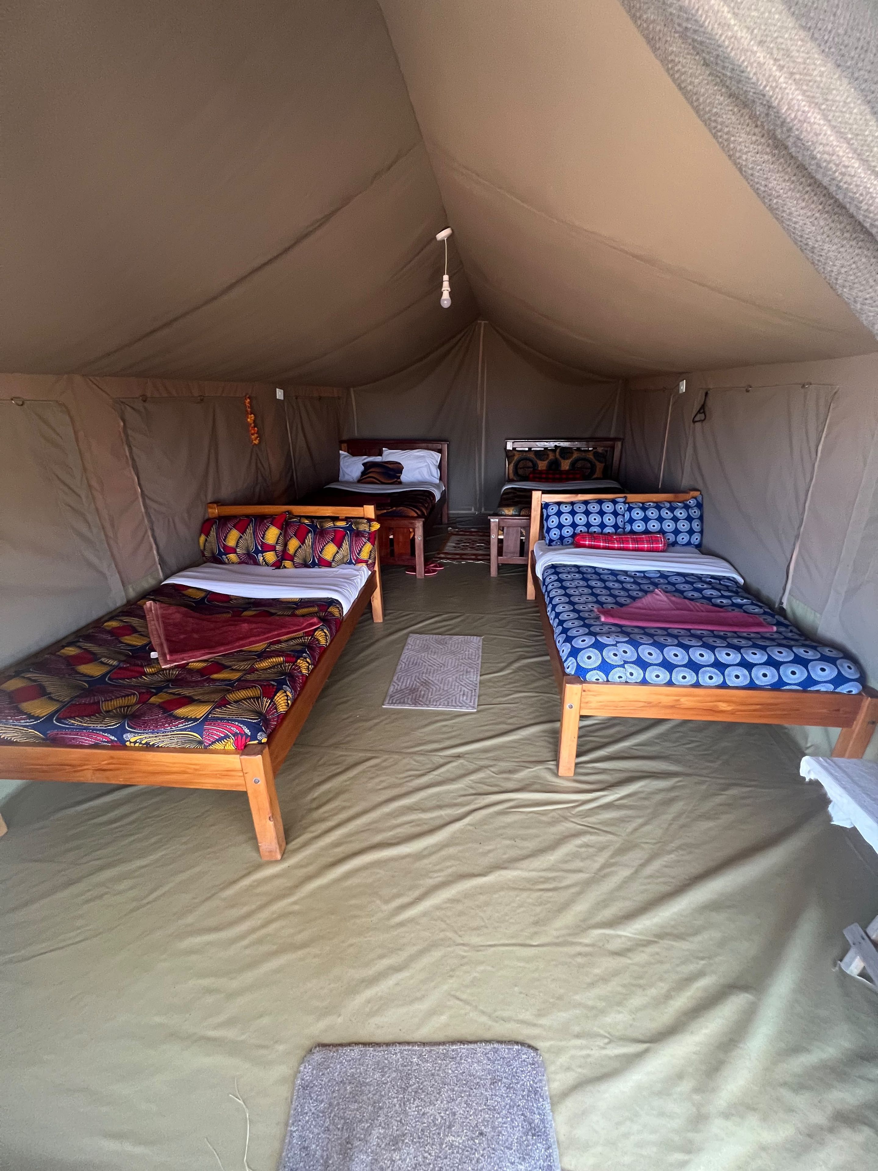 A tent with two beds, a table, and a hanging light fixture.