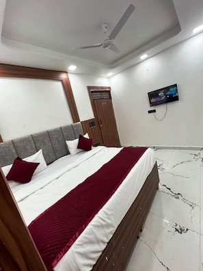 Habitación de hotel con cama, televisión montada en la pared y ventilador de techo.