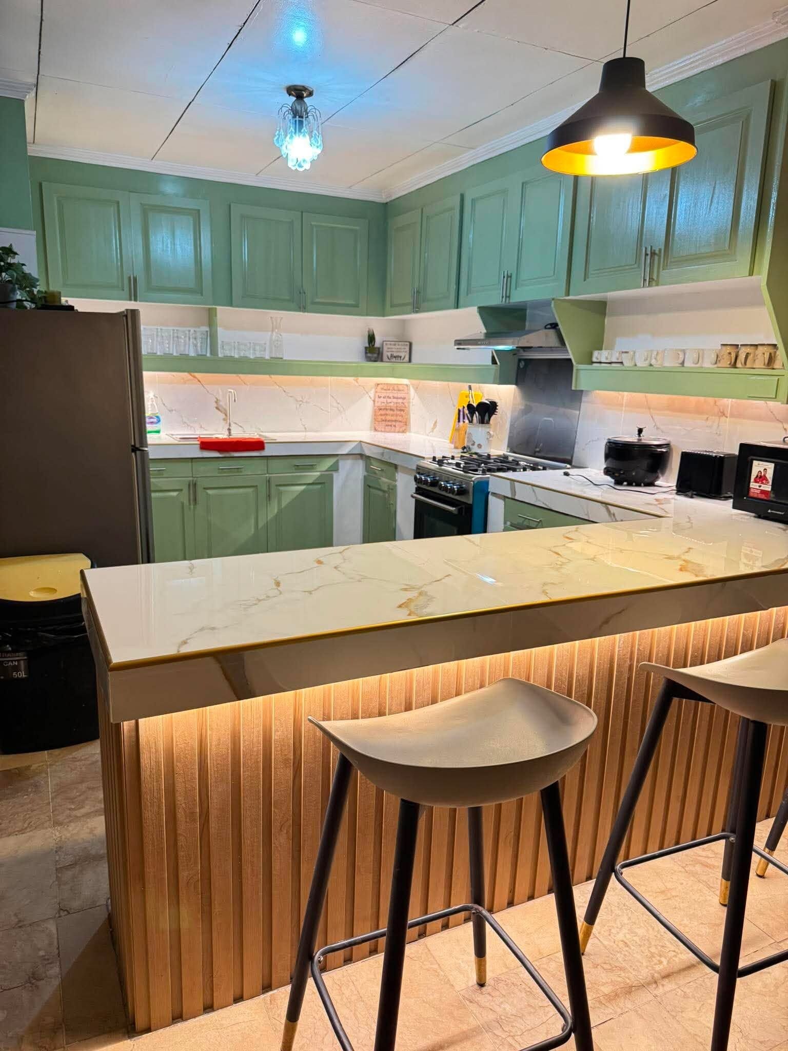 A kitchen with green cabinets, a marble countertop, a gas stove, and a pendant light.