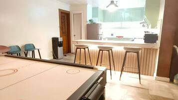 A pool table in a room with a kitchen area, bar stools, and a door leading to another room.