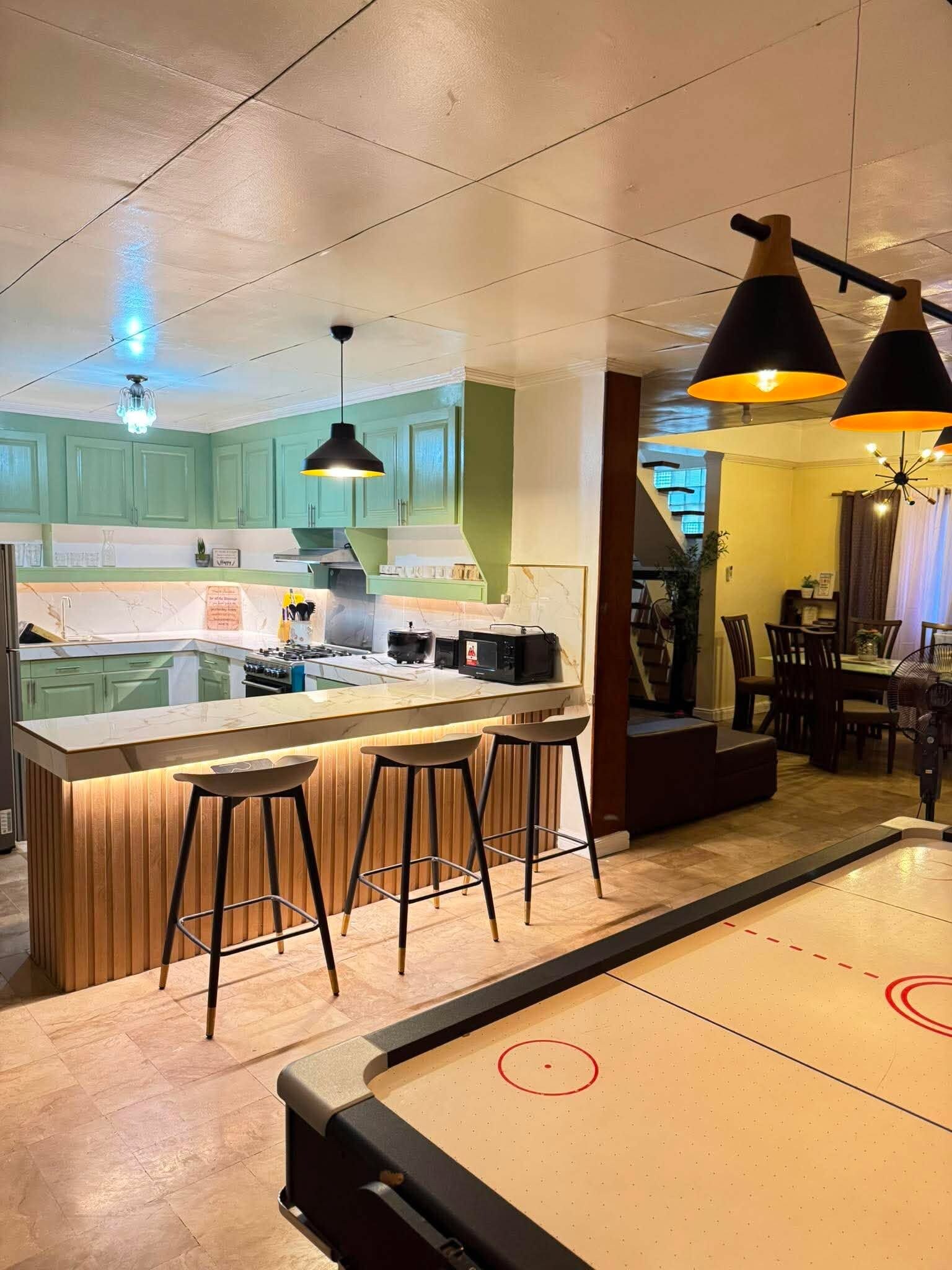 A modern kitchen with a central island, bar stools, pendant lighting, and a dining area with a table and chairs.