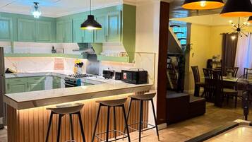 A modern kitchen with a central island, bar stools, pendant lighting, and a dining area with a table and chairs.