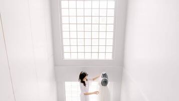 A room with a large window, a person holding a dress, and a mirror.