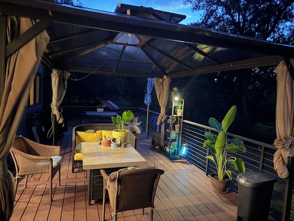 An outdoor patio with a table and chairs, surrounded by potted plants and a covered area.