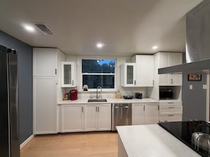 Een moderne keuken met witte kasten, roestvrijstalen apparatuur, een raam en een aanrecht.