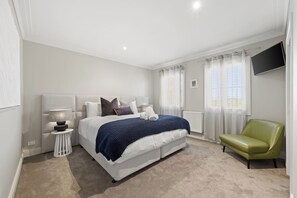 A bedroom with a bed, a nightstand, a lamp, a chair, and a TV. - Stylish Ballarat Group Escape | Sleeps 10 (Lake Gardens)