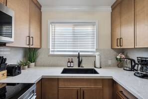 A modern kitchen with wooden cabinets, a stainless steel sink, a window with blinds, and various kitchen appliances. - Cozy and Modern 1 Bed 1 bath Travelers Dream Home in Downtown Mountain View (Mountain View)