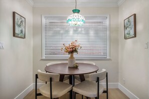 Un coin repas comprenant une table ronde, quatre chaises, un vase avec des fleurs et un luminaire décoratif suspendu au-dessus.