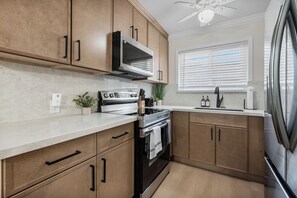 Une cuisine avec des meubles en bois, une cuisinière en acier inoxydable, un four encastré et une fenêtre avec des stores.