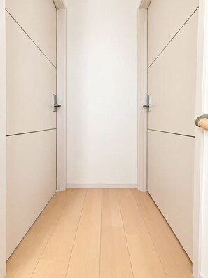 A narrow hallway with white walls and wooden flooring, leading to a door with a metallic handle. - Tokyo Koiwa | Private 2-Bedroom Stay for 5 Guests (江戸川区東小岩5-25-14)