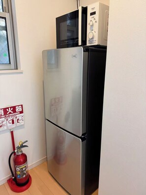 A kitchen with a stainless steel refrigerator, a microwave, and a red fire extinguisher on the floor. - Tokyo Koiwa | Private 2-Bedroom Stay for 5 Guests (江戸川区東小岩5-25-14)