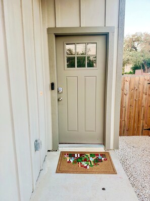 A beige front door with a peephole, a mail slot, and a doormat with holiday decorations. - Newly Built 3-bedroom modern house with parking in vibrant Downtown San Antonio (San Antonio)
