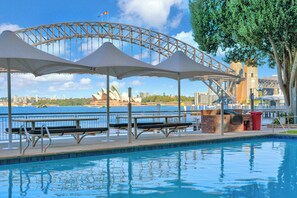 A swimming pool with benches and umbrellas, a view of the Sydney Opera House, and a bridge in the background. - 1BR Harbour View Nest Opal (McMahons Point)