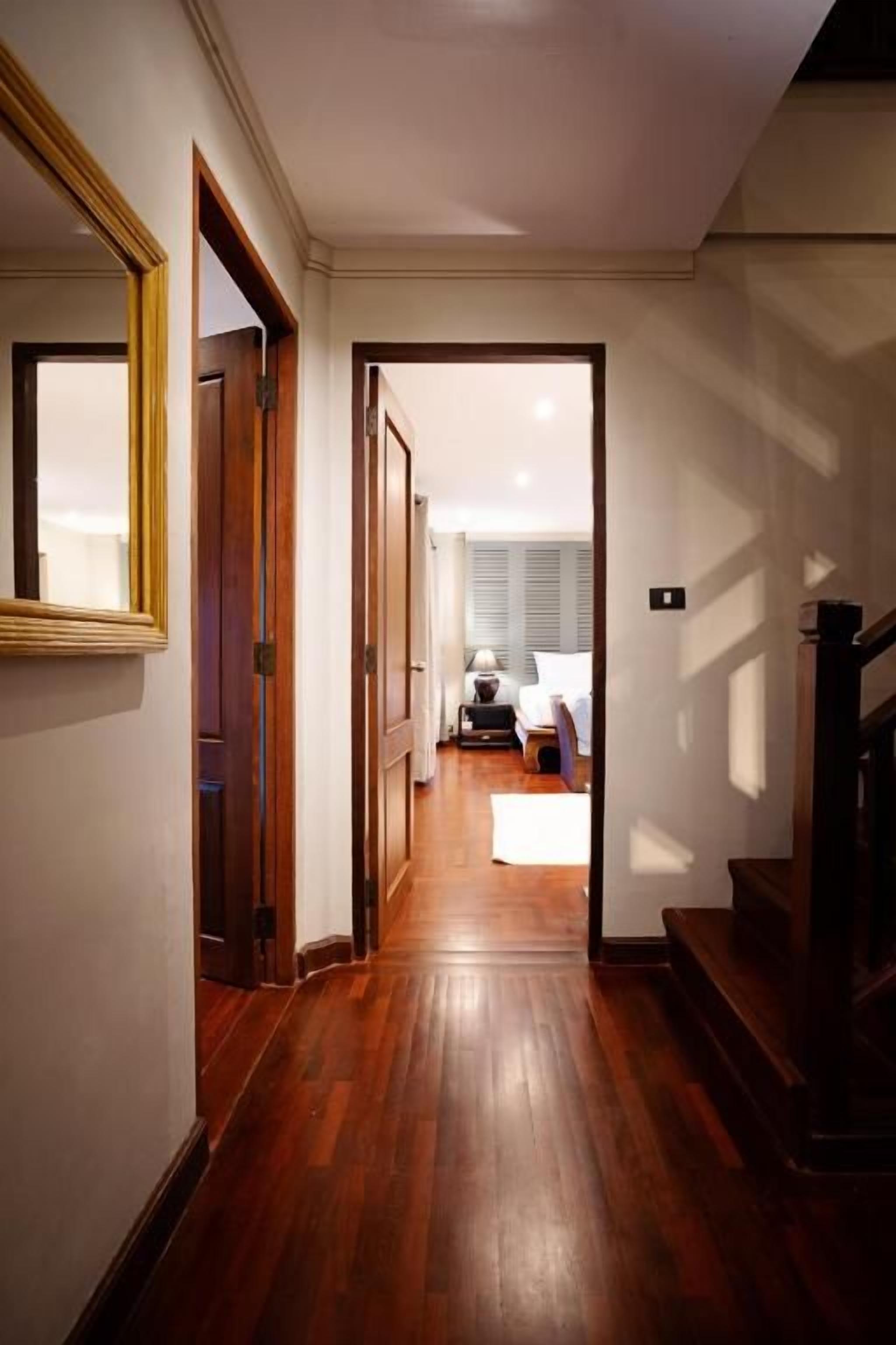 Un pasillo con piso de madera que conduce a una habitación con una cama y una mesita de noche.