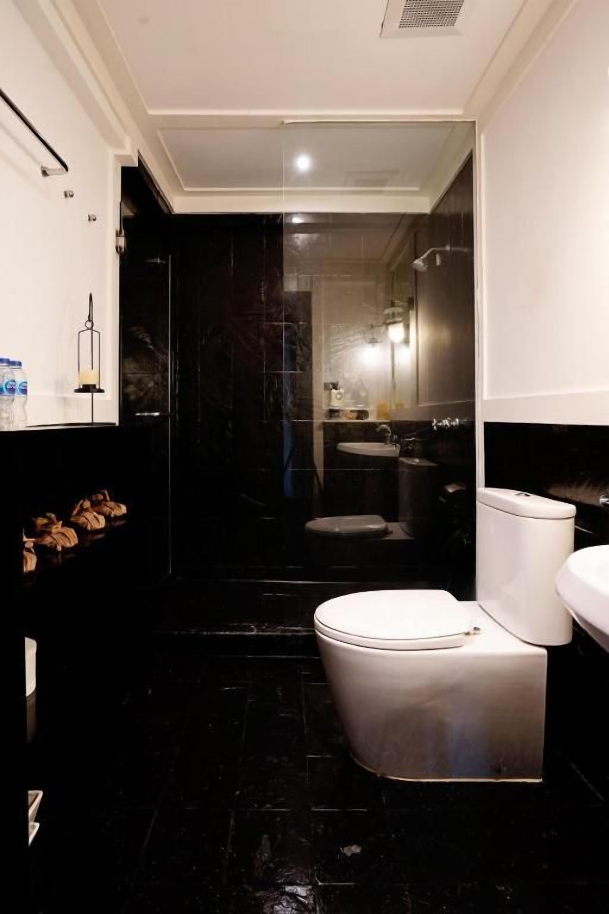Un baño moderno con inodoro blanco, lavabo negro y espejo.