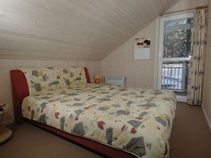 A bedroom with a bed, a red chair, a lamp, a radiator, and a window with a view of trees. - Holiday Home Seebar (Ostseebad Baabe)