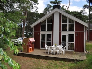 A wooden deck with a dining table and chairs, a wicker chair with a striped cover, and a car parked nearby. - Holiday Home Seebar (Ostseebad Baabe)