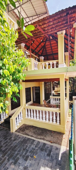 A two-story building with a balcony, a tiled roof, and a garden area with plants. - Cozy Homestay Steps Away from Alappuzha Beach (Alappuzha)