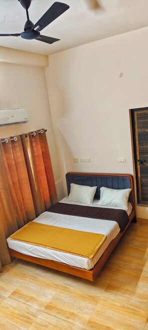 Une chambre à coucher avec un lit, un ventilateur de plafond, un appareil de climatisation et une fenêtre avec des rideaux.
