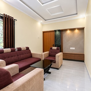 A modern living room with a sofa set, a glass coffee table, and a wooden cabinet. - Hotel The Pavilion (Tadepalle)