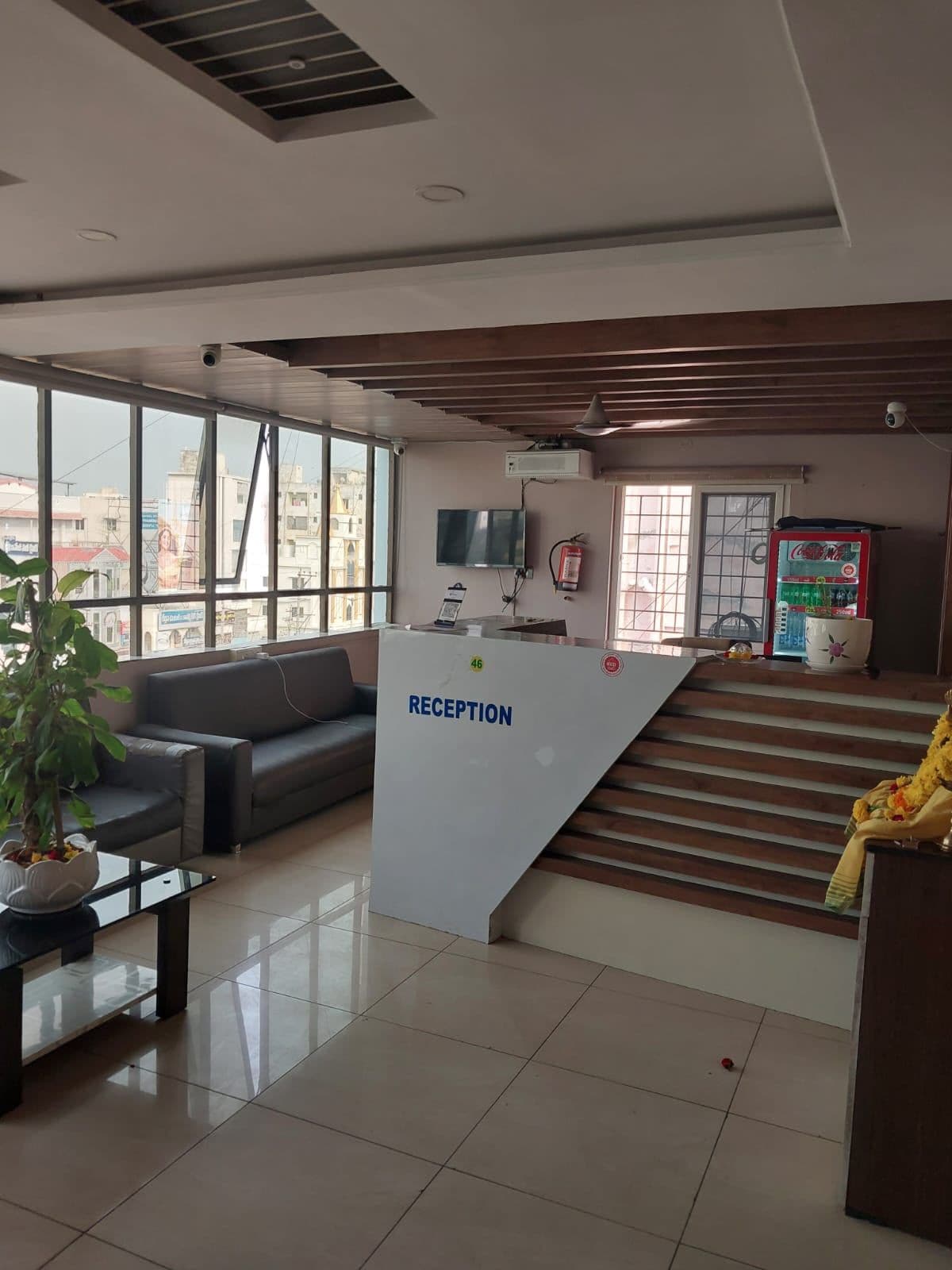 A reception area with a reception desk, a sofa, a potted plant, a television, and a fire extinguisher.