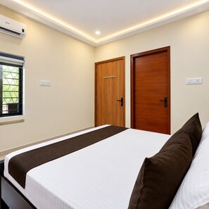 Una habitación de hotel con una cama, dos puertas de madera, una ventana con reja de metal y un equipo de aire acondicionado en la pared.
