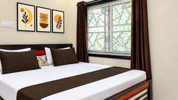 Habitación de hotel con cama, unidad de aire acondicionado, ventana con cortinas y decoración en la pared.